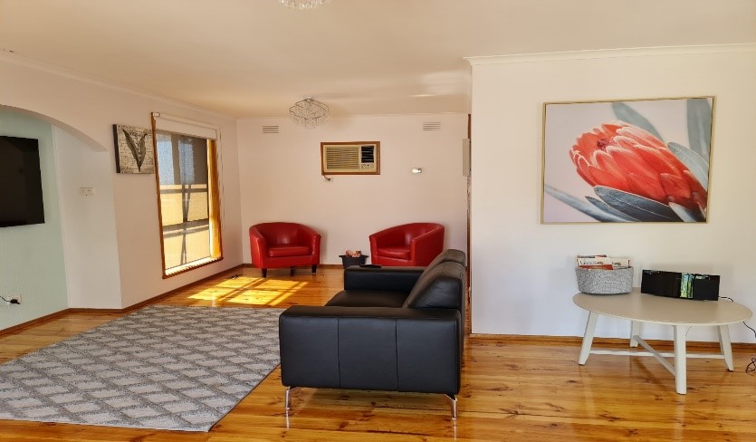 Open plan living area with floorboards, black leather couch with red learther chairs, with large photograph of banksia flower on wall