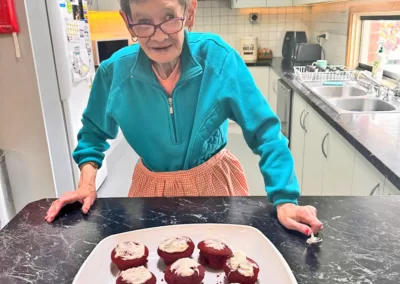 An elderly woman stands at a kitchen bench and inspects the set of cakes she’s baked