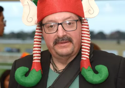 A standing man wears an elf hat and Christmas t-shirt.