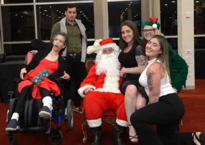 Santa sits with three women seated to the left, another woman seated to the right, and a man in the background.