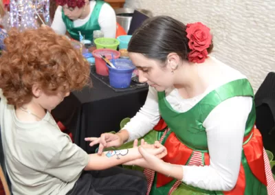 A woman dressed in elf costume paints the arm of a seated boy.