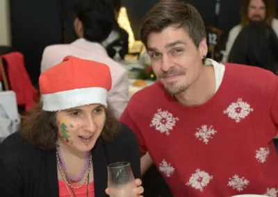 A man in a red Christmas-themed jumper sits with a woman wearing a Santa hat.