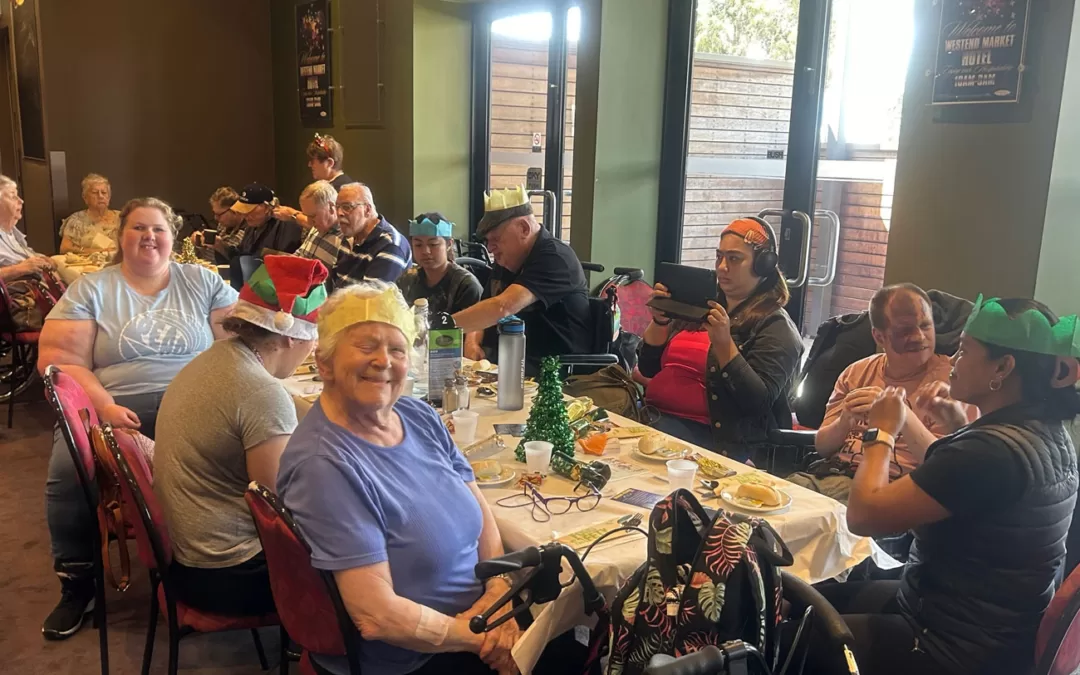 A group of people enjoy Christmas lunch at a long table.