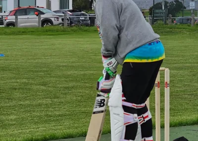 A woman faces up to bat in a cricket match, smiling beneath her helmet