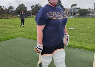 A woman smiles under her helmet while holding her cricket bat.