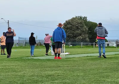 Several people stand on a cricket ground, engaged in a match.