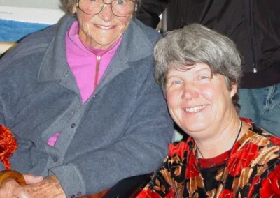 An older woman sits slightly above a middle-aged woman, both smiling.
