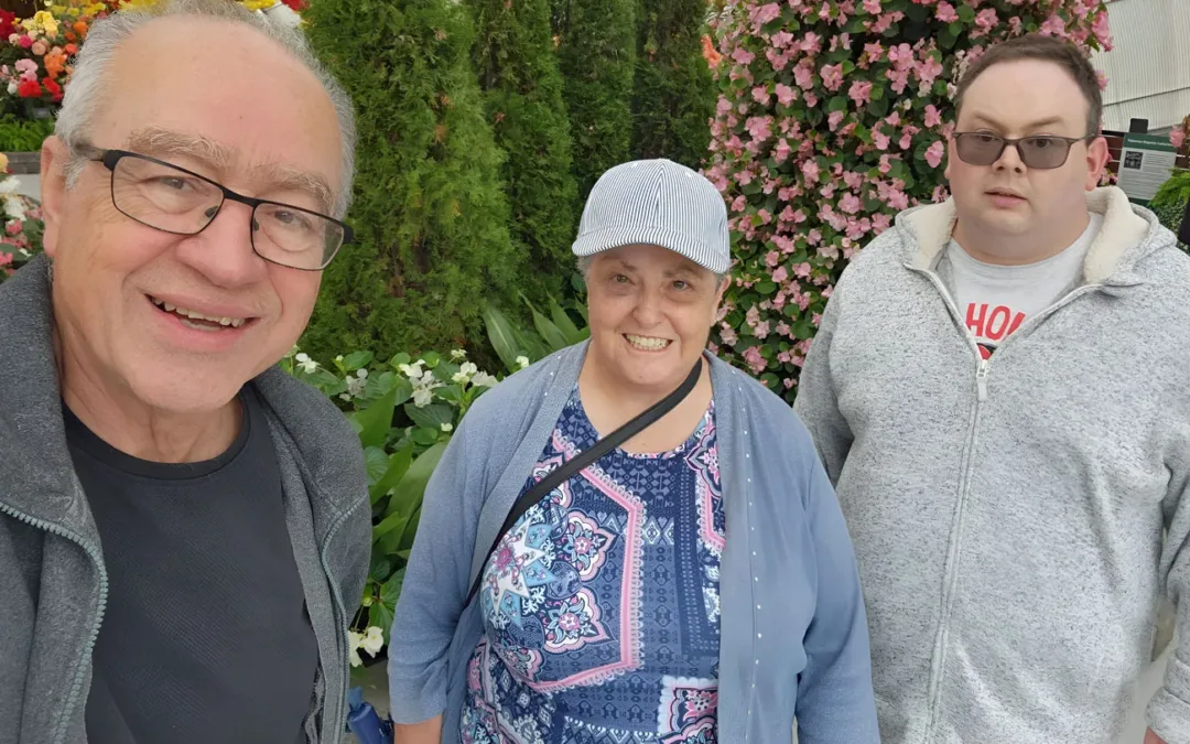 Three people smile for the camera: on the left, a middle-aged man; in the centre, a middle-aged woman; on the right, a younger man.