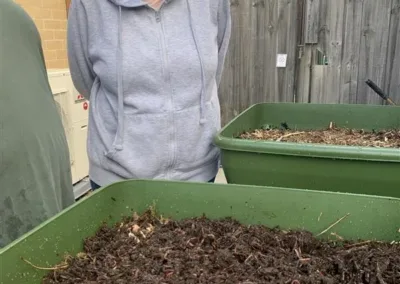 A woman inspects a large bin full of dirt with worms in the top soil.