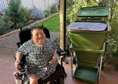 A woman sitting in a wheelchair next to a compost bin.