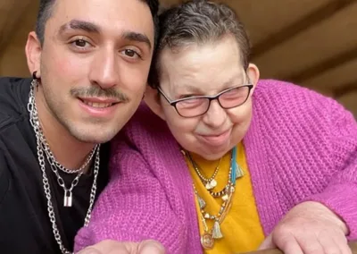 A woman holds a wood railing while a young man smiles beside her.