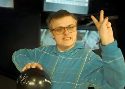 A man gives a two-finger peace salute as he holds a tenpin bowling ball.