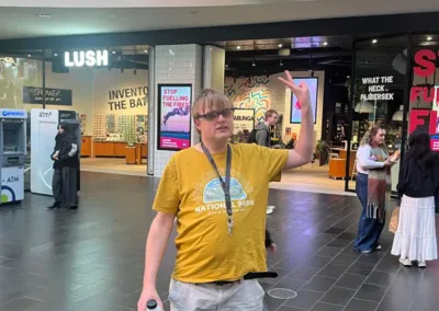 A man stands with arms raised in a shopping centre in front of a large clock.