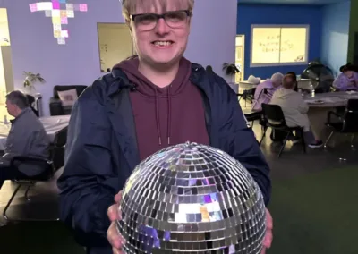 A man smiles wearing a cardboard crown as he holds a large disco ball.