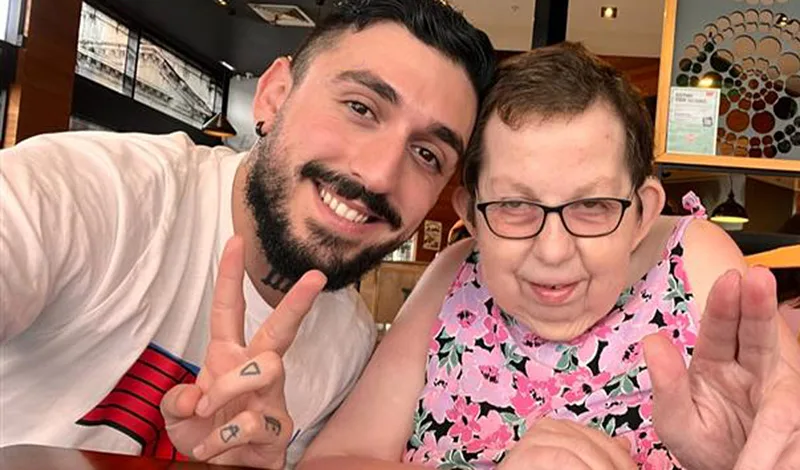 A bearded man and older woman smile and wave to the camera.